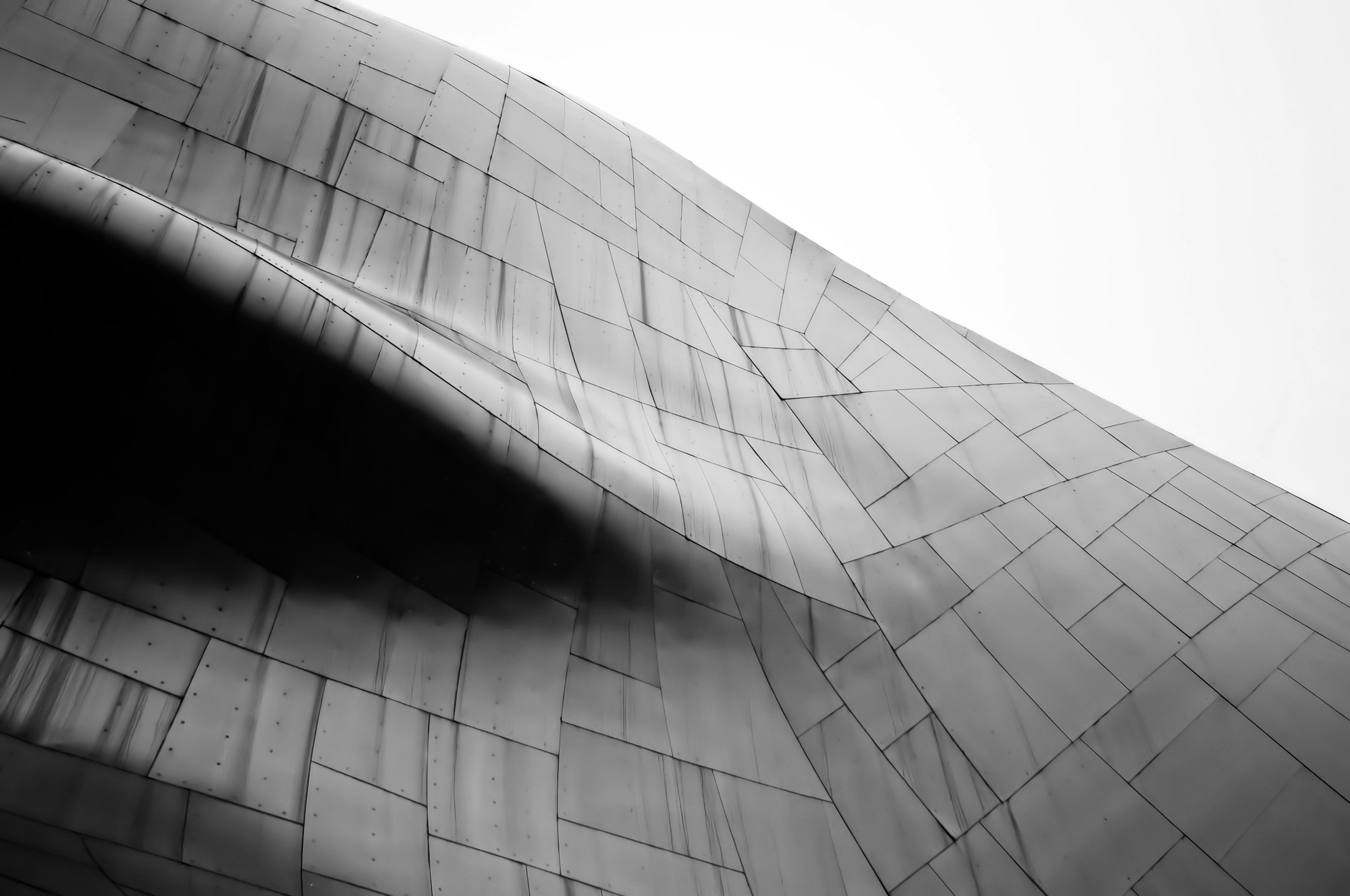 Abstract close-up of a curved metallic building facade with geometric panel seams, black and white, sleek modern mood